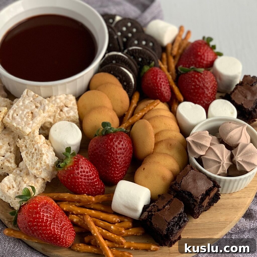 A serving board filled with amzing items such as mini rice krispies, mini brownie bites, safe oreos, pretzels, vanilla wafers, large marshmallows, strawberries and a small bowl of chocolate ganache dipping sauce. 